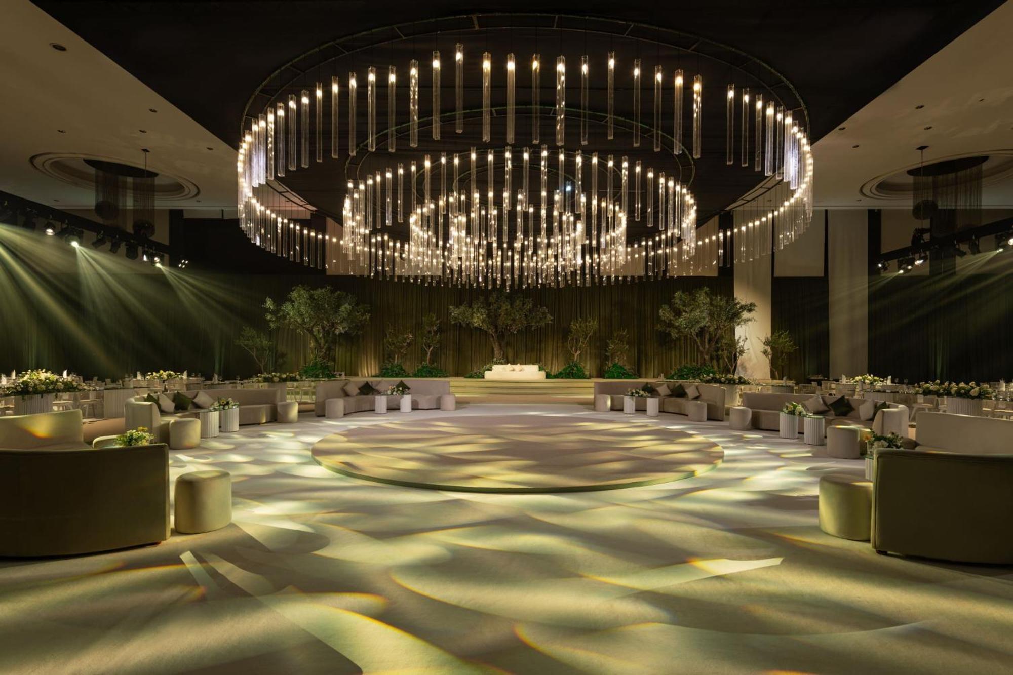 Le Meridien Dubai Hotel & Conference Centre Exterior foto The photo shows an elegantly designed event space with a spacious layout. A large, circular chandelier hangs prominently from the ceiling, adorned with multiple lights that create a dramatic illumination effect. The room is illuminated with soft ligh