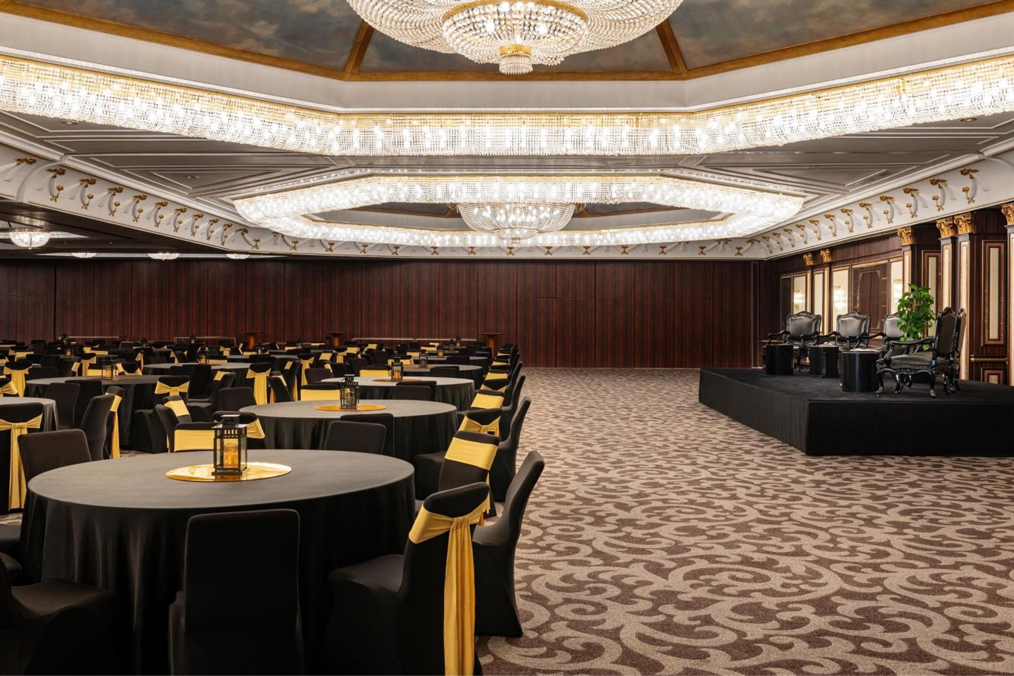 Le Meridien Dubai Hotel & Conference Centre Exterior foto The photo depicts an elegant banquet or event hall. The room features a spacious interior with a plush carpet and a decorative ceiling adorned with a large chandelier. There are several round tables covered with black tablecloths, each topped with a 